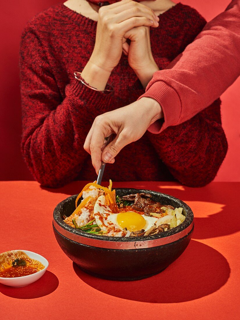 Bibimbap (a colourful rice bowl with beef, vegetables and a fried egg, Korea) being stirred