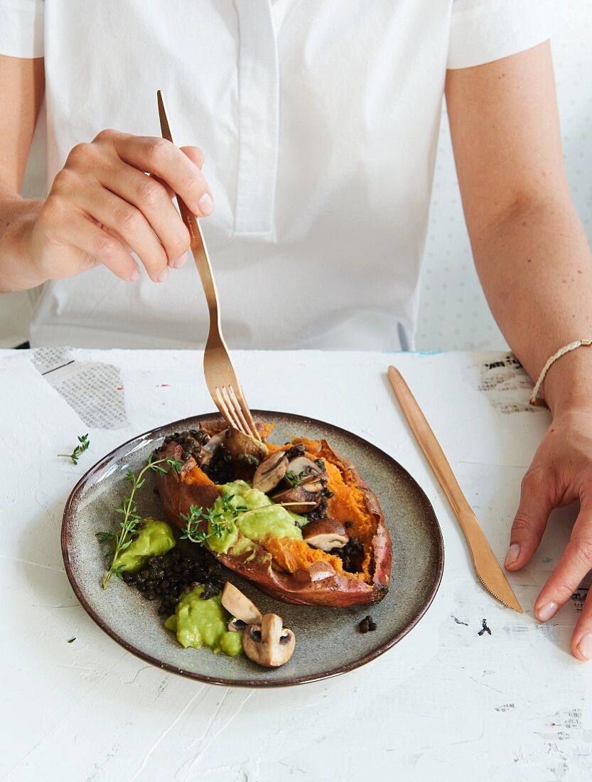 An oven-baked sweet potato filled with beluga lentils, avocado and mushrooms