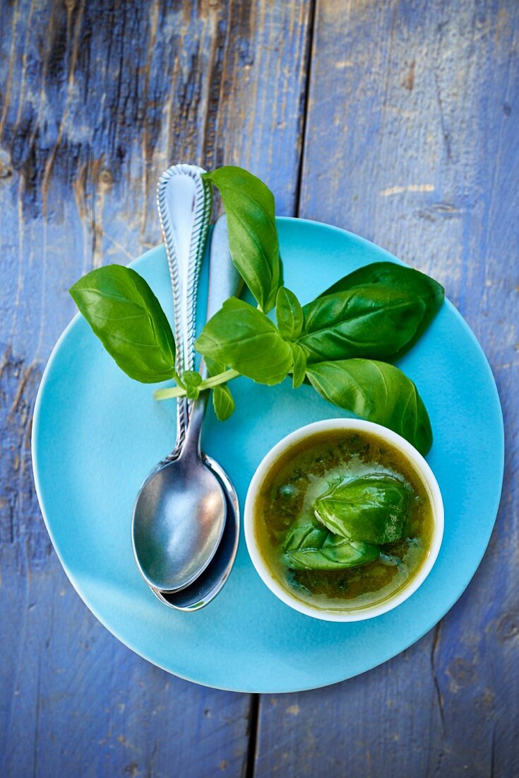 Basil vinaigrette in a small bowl, basil leaves and a spoon on a blue plate