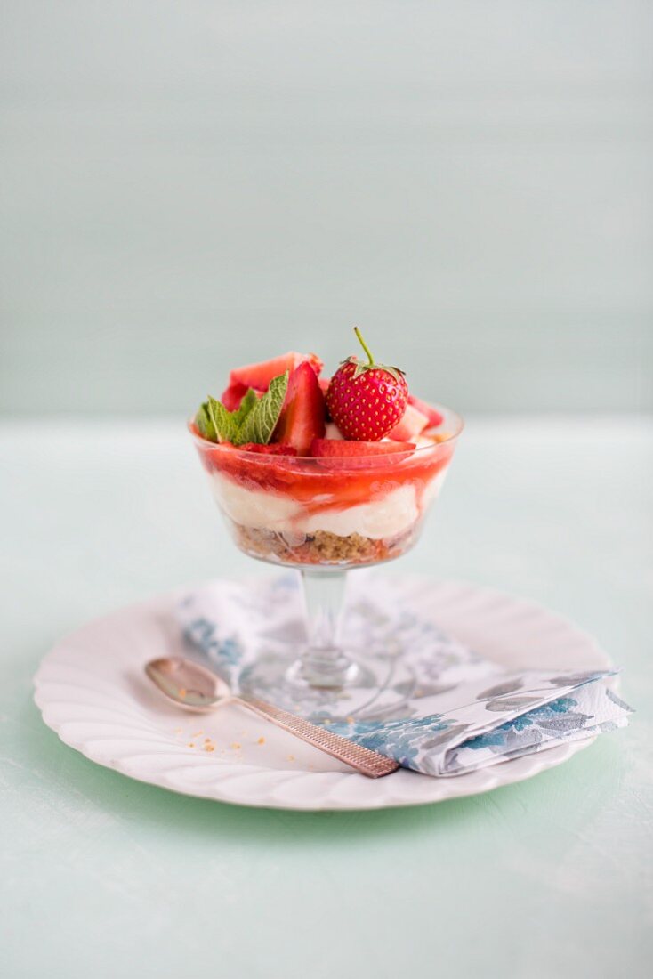 Strawberry and vanilla cheesecake with nut and biscuit base in a glass