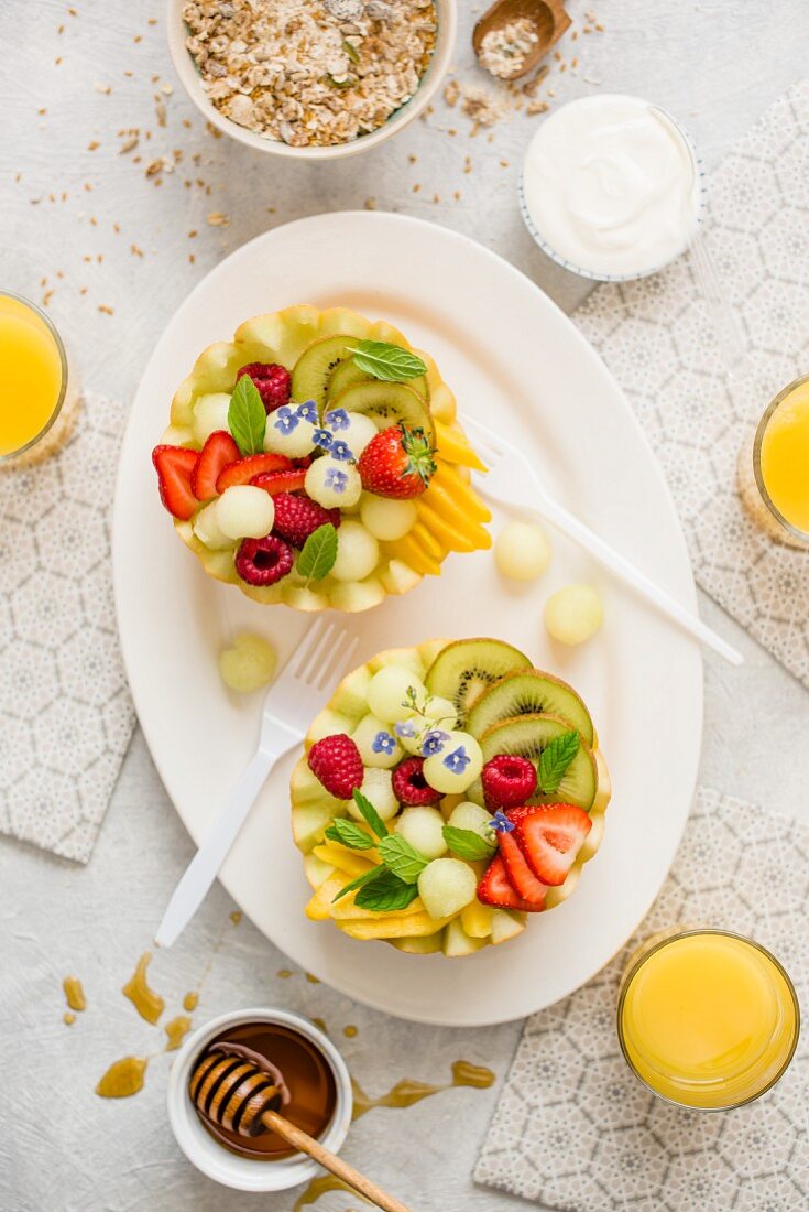 A healthy breakfast: fruit salad served in melon halves, yoghurt, granola, orange juice and honey