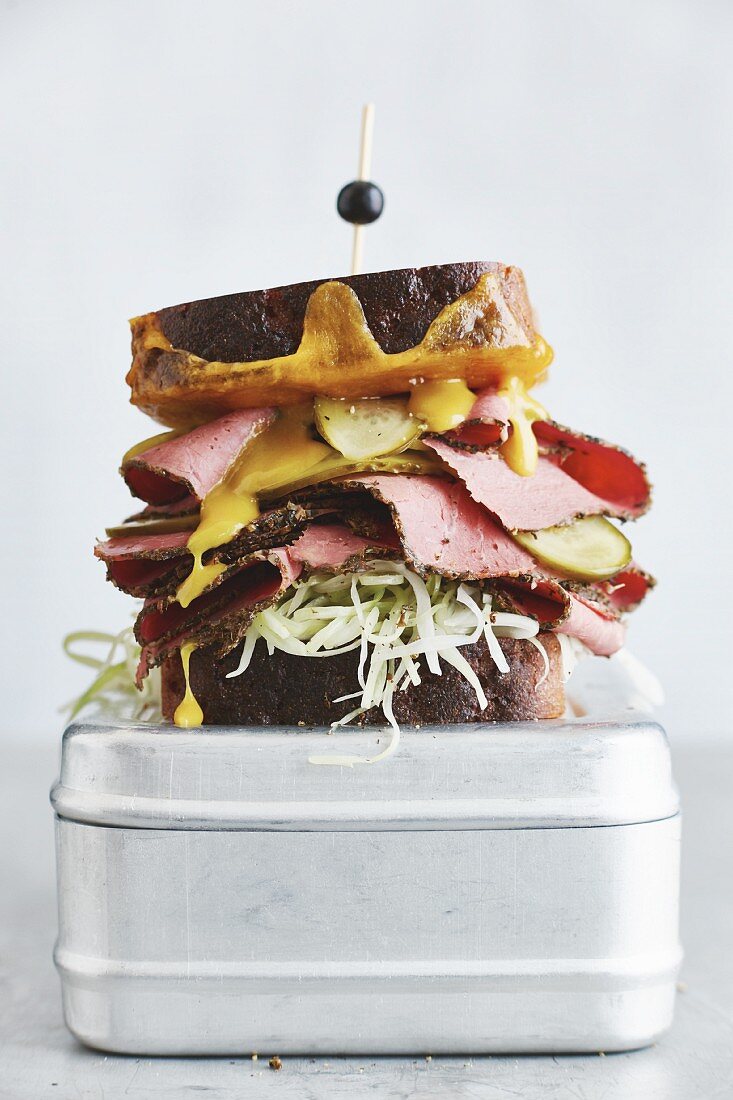 A pastrami sandwich with cheddar, coleslaw and gherkins