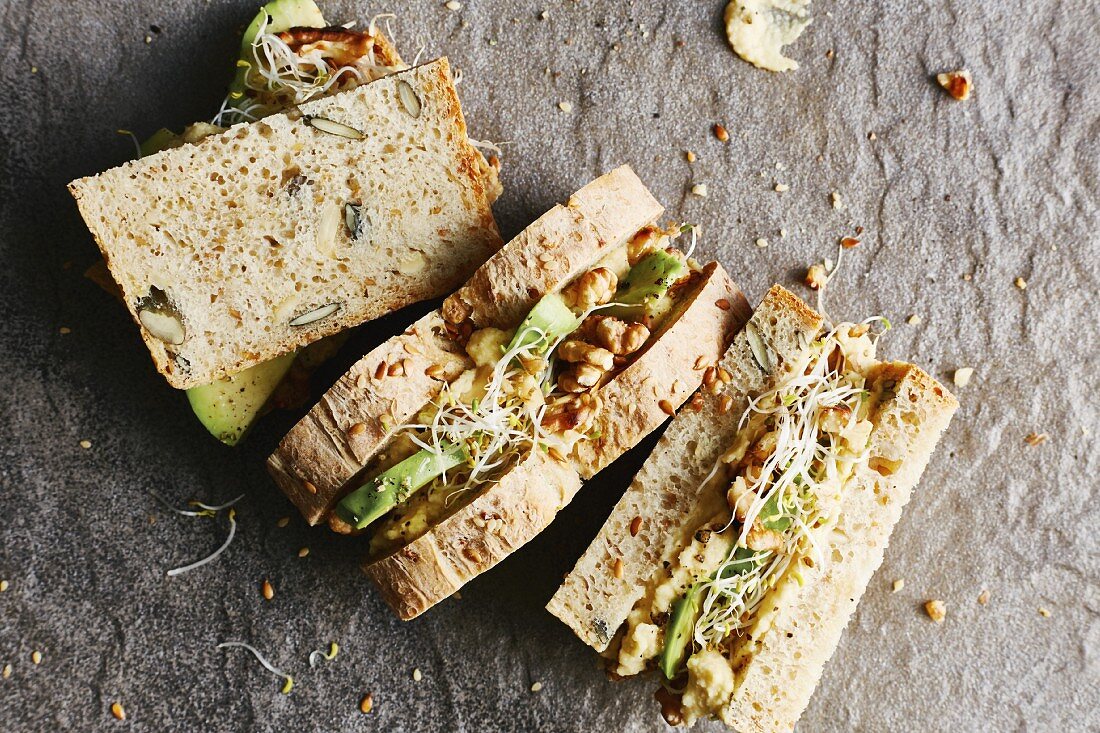 Sandwiches on seed bread with apple and chickpea spread, avocado, alfalfa sprouts and walnuts