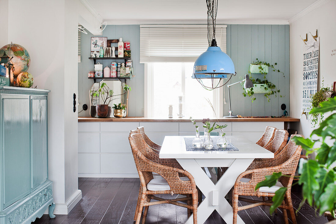 White dining table, rattan chairs and cabinet painted pale blue in open-plan interior