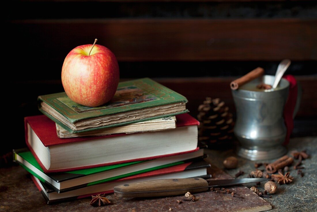 A Pink Lady apple on a pile of old books with mulled apple juice