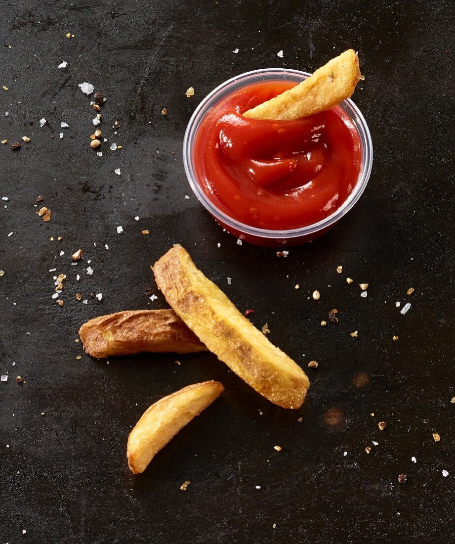 Four French fries on a black baking tray with tomato ketchup