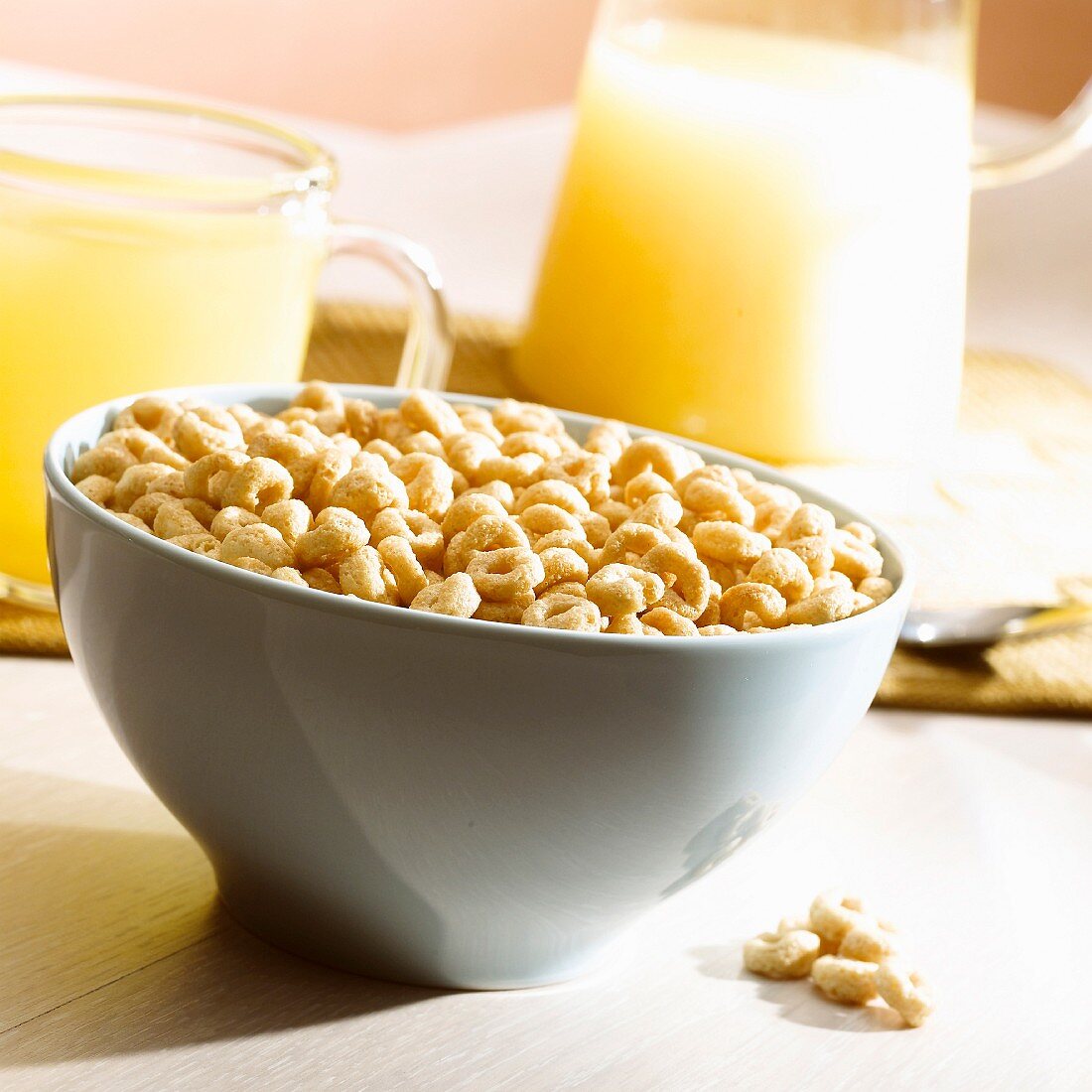 A cup full of ring-shaped cereal and glasses of orange juice