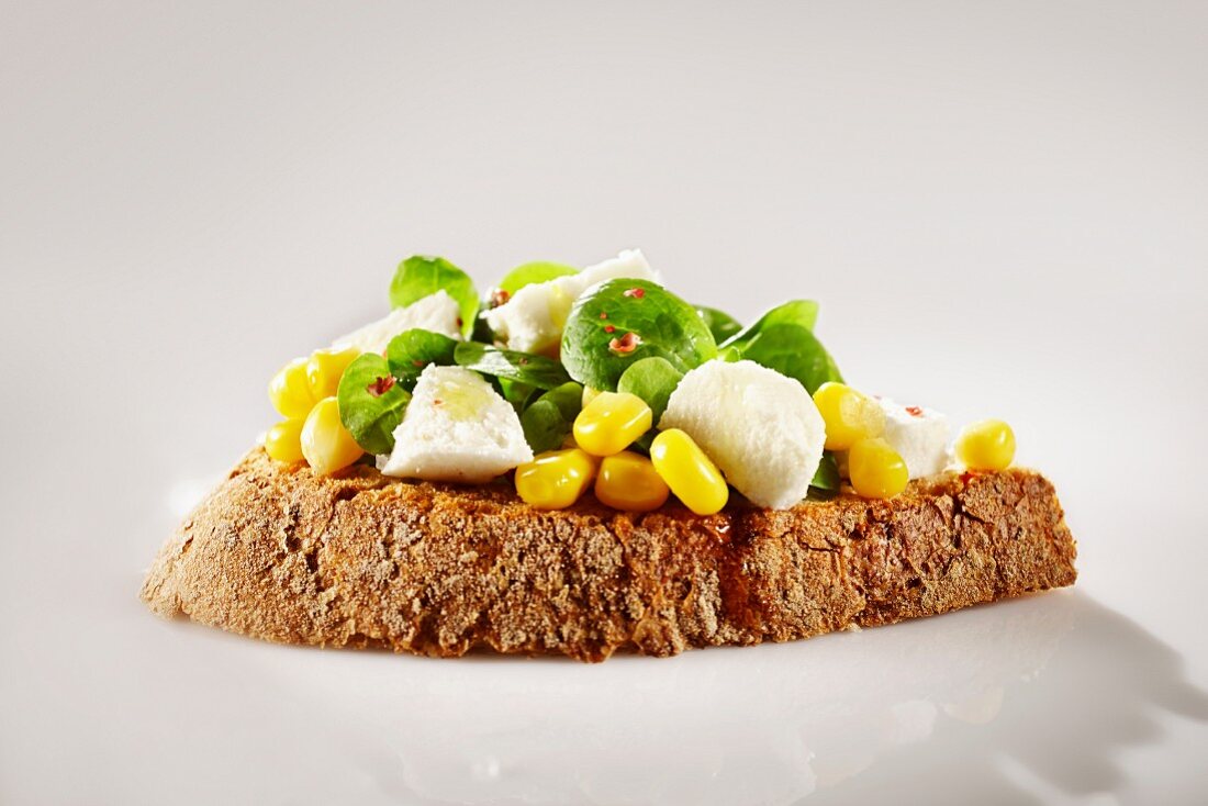 Belegtes Landbrot mit Feldsalat, Mozzarellawürfeln, Mais und rosa Pfeffer