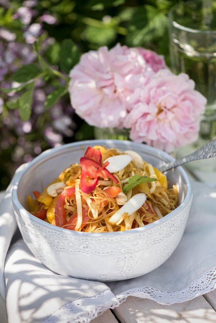 Singapore noodles with yellow pepper, chilli and shoots on a table outdoors