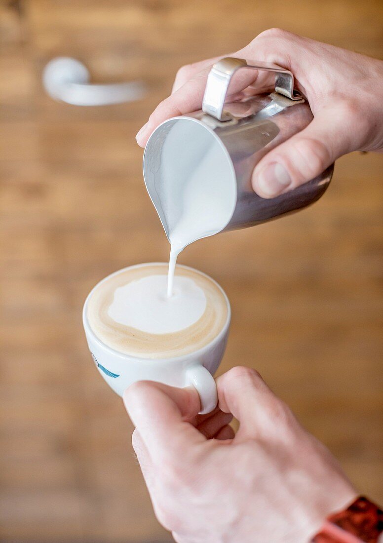 A barista pouring frothed milk into a cappuccino cup