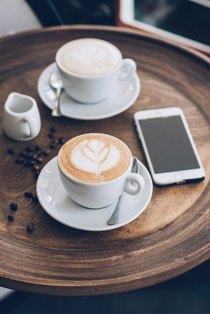 Zwei Tassen Cappuccino neben Smartphone auf Tisch im Café