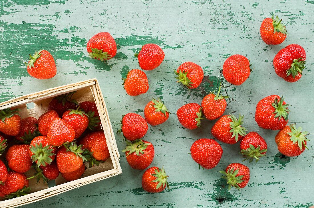 Strawberries inside and next to a wood basket on a wooden table