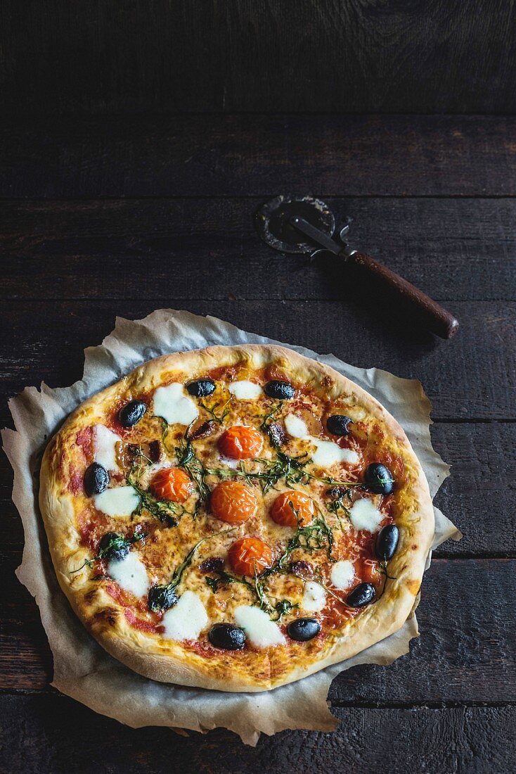 Pizza mit Mozzarella, Oliven und Kirschtomaten auf Holzuntergrund