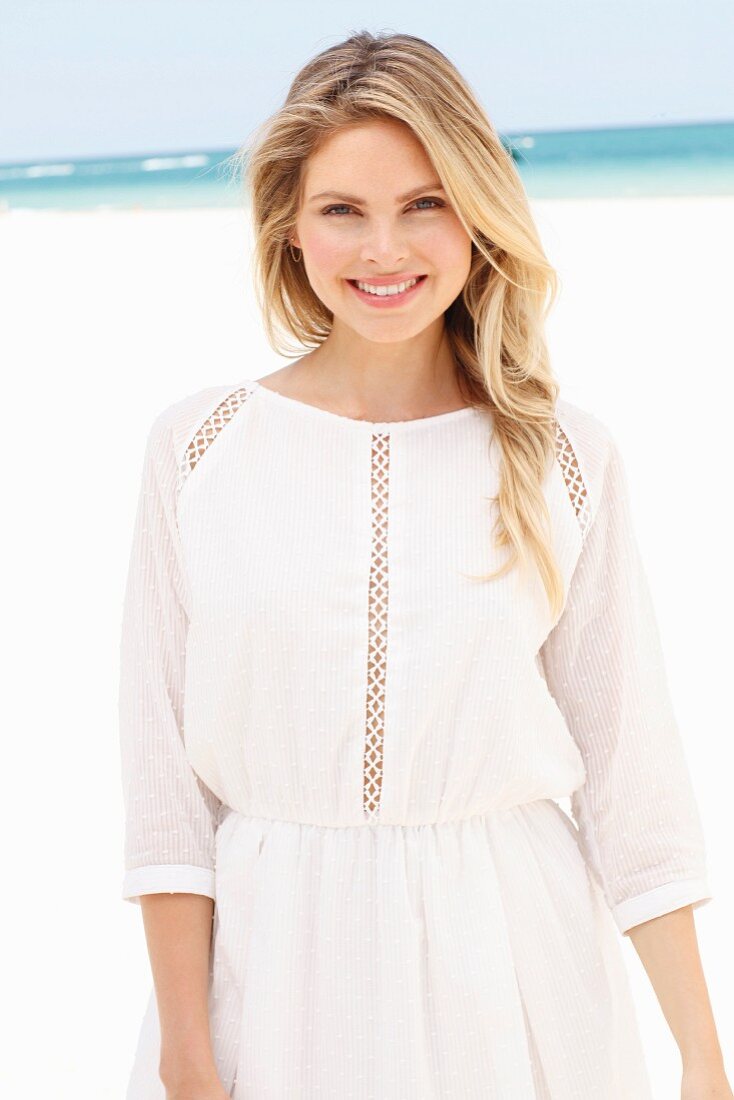 A blonde woman wearing a white summer dress with lace panel on the beach