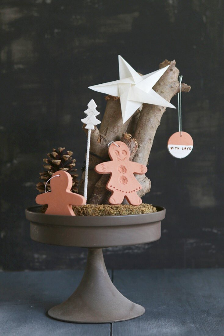 Christmas arrangement of gingerbread men made from clay and paper star on cake stand