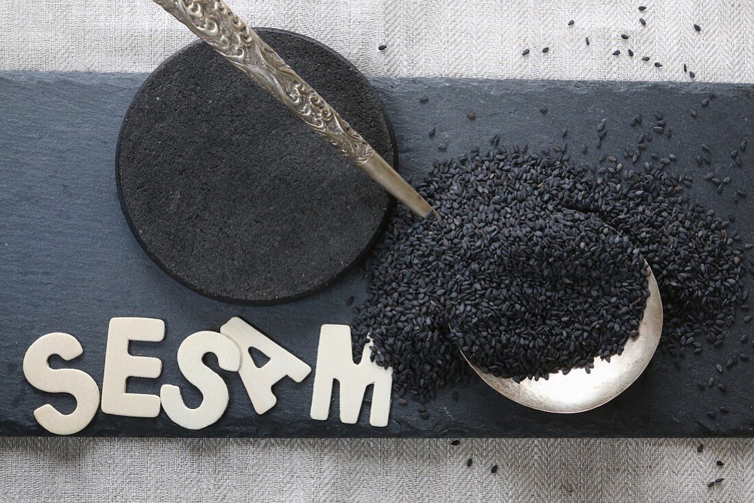 Black sesame seeds on a silver spoon and wooden letters on a slate plate