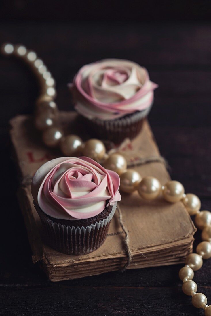 weiße Rosen-Cupcakes auf Buch mit Perlenkette