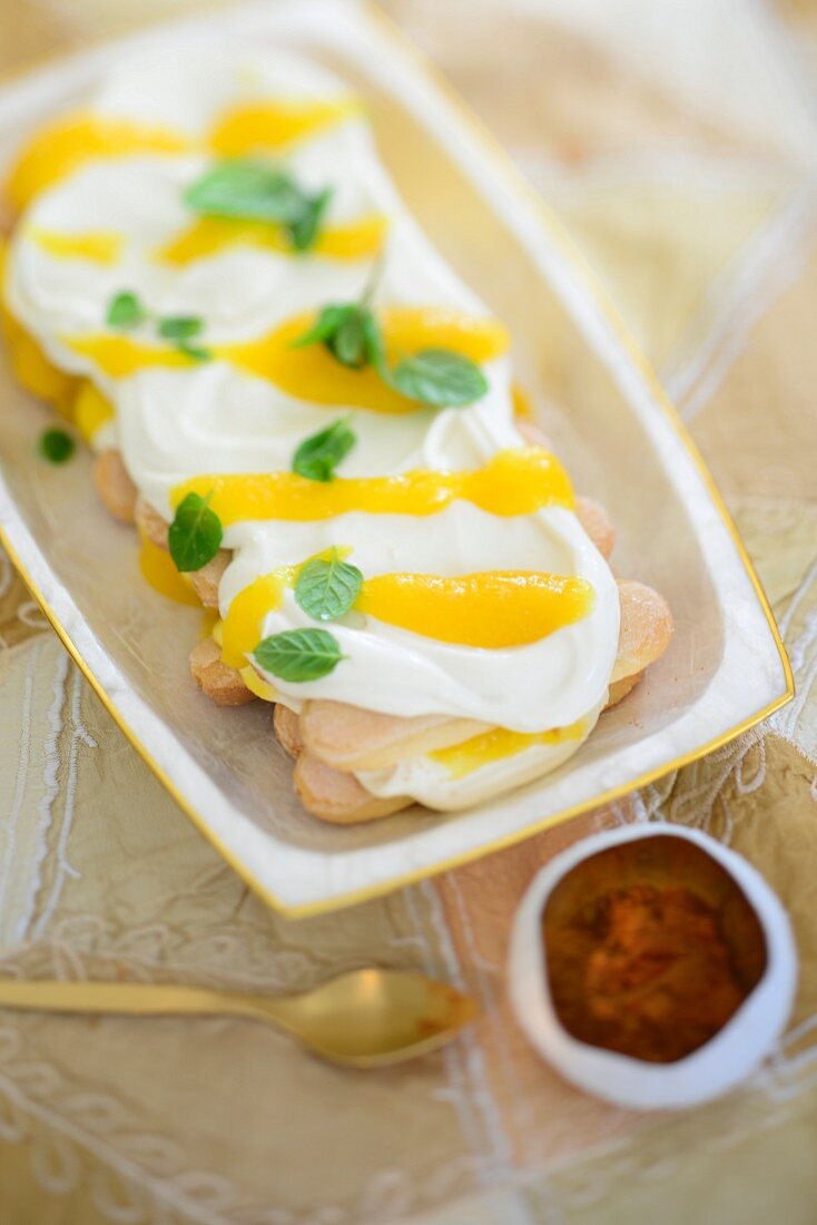 A layered dessert with sponge biscuits, whipped cream and mango sauce