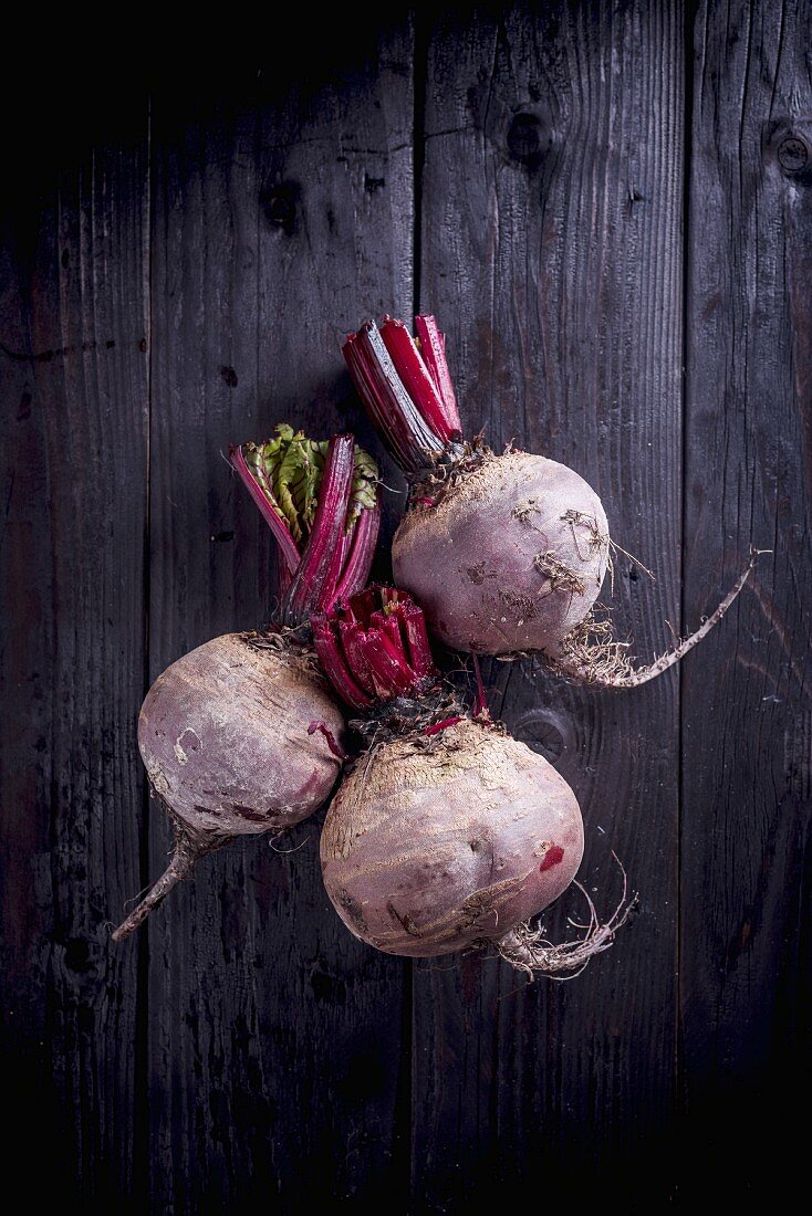 Three beetroots on a black wooden background (seen from above)