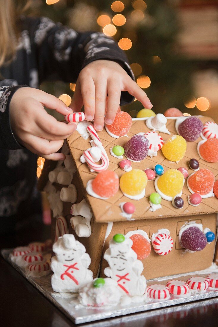 Mädchen verziert Lebkuchenhaus mit Süßigkeiten