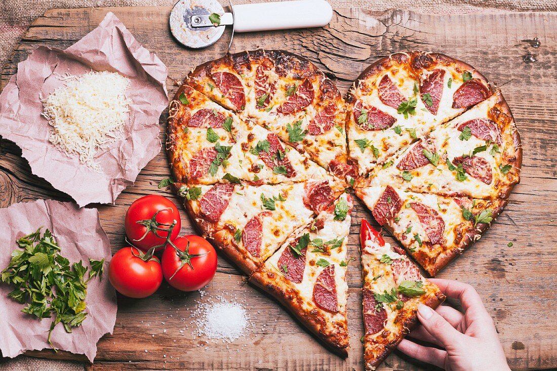 A hand taking a slice from a heart shaped pizza