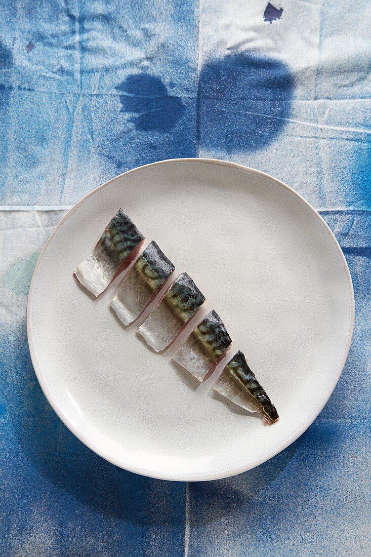 A raw mackerel cut into pieces on a plate (top view)