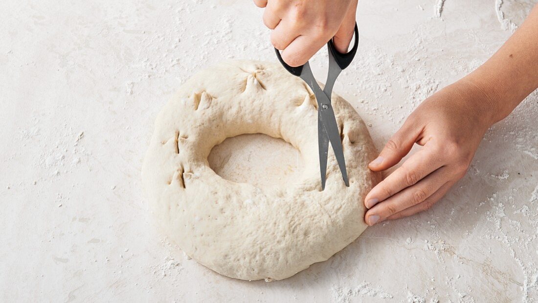 Cutting an wreath of bread dough with scissors