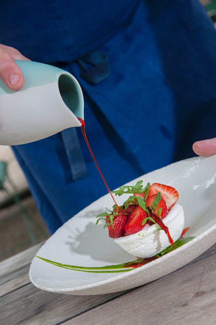 A meringue nest with strawberries, rocket, and strawberry sauce