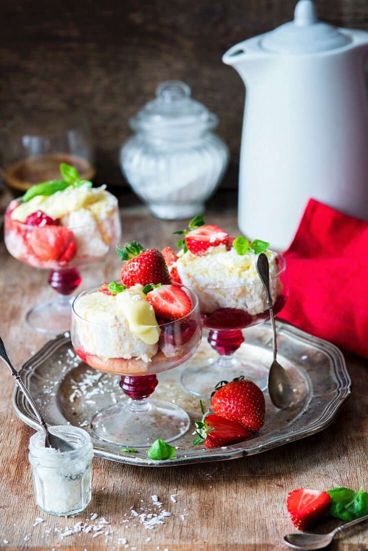 Kokos-Baiserrolle in Stücke geschnitten serviert mit Erdbeeren in Dessertgläsern