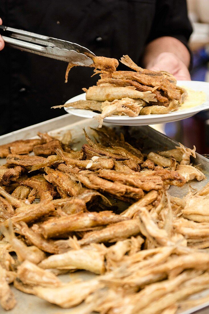 Using kitchen utensils to serve fried smelt onto a plate (Northern Germany)