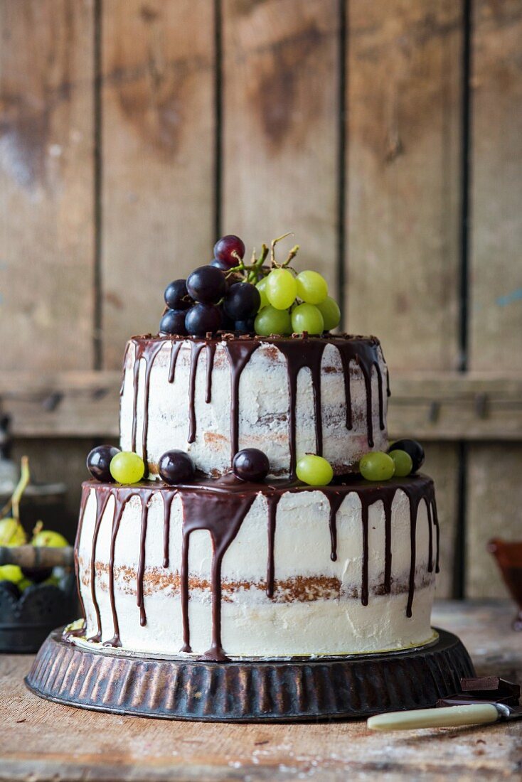 A two tier buttercream cake with grapes and a chocolate glaze
