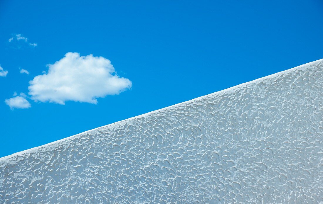 Blauer Himmel mit Wolke über diagonaler, weißer Mauer