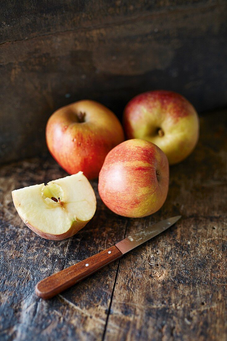 Ganze und aufgeschnittene Boskop-Äpfel mit Messer auf Holzuntergrund