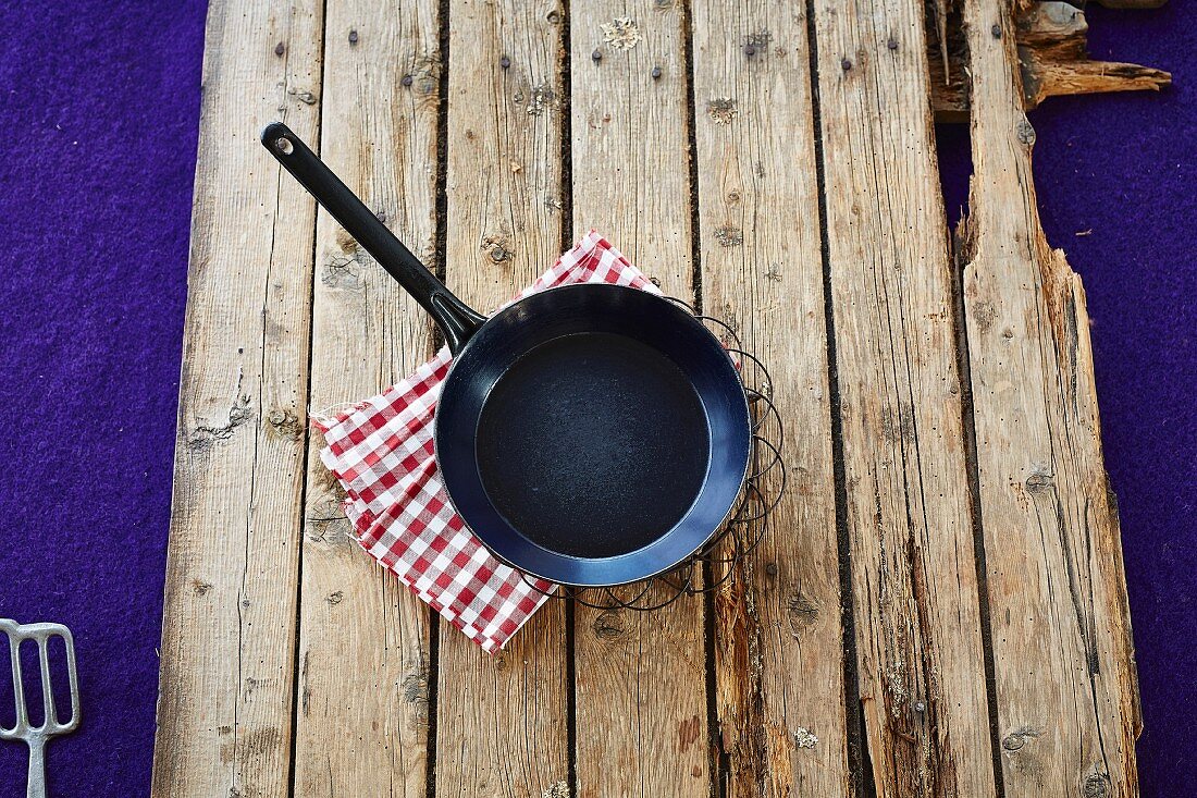 A frying pan and a checkered cloth on a wooden background