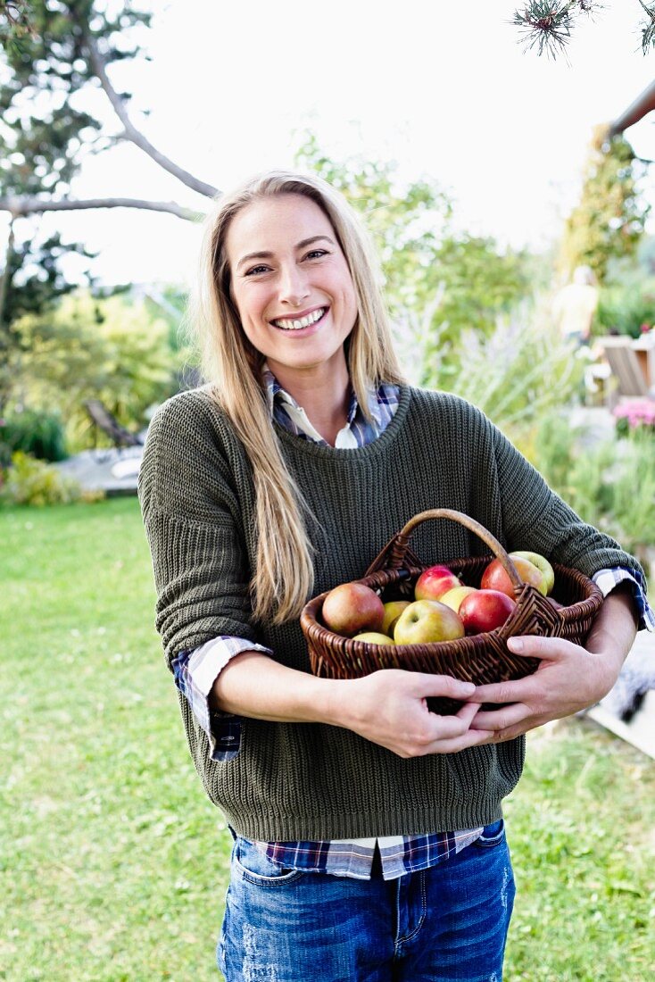 A blonde woman with a basket of fresh apples in a garden