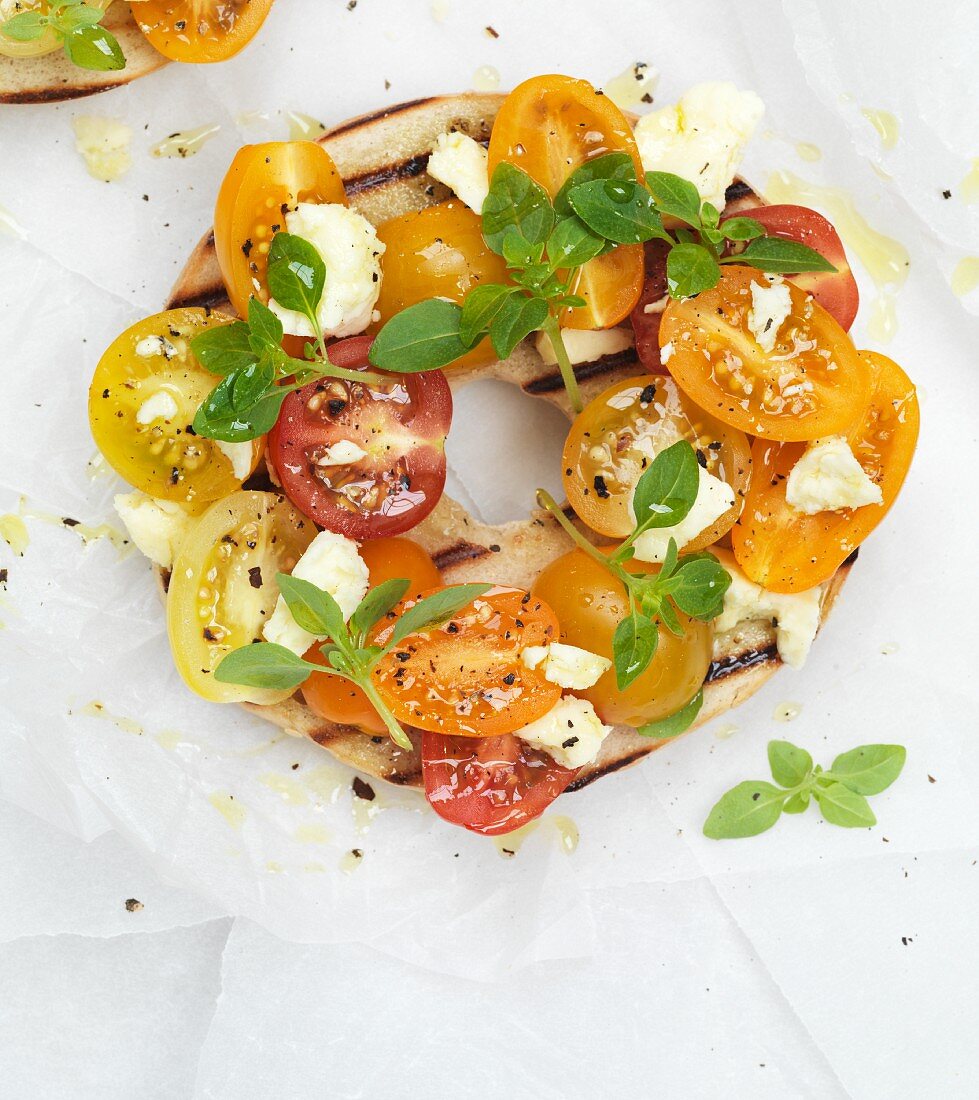 A grilled bagel with cherry tomatoes and feta cheese (top view, close up)