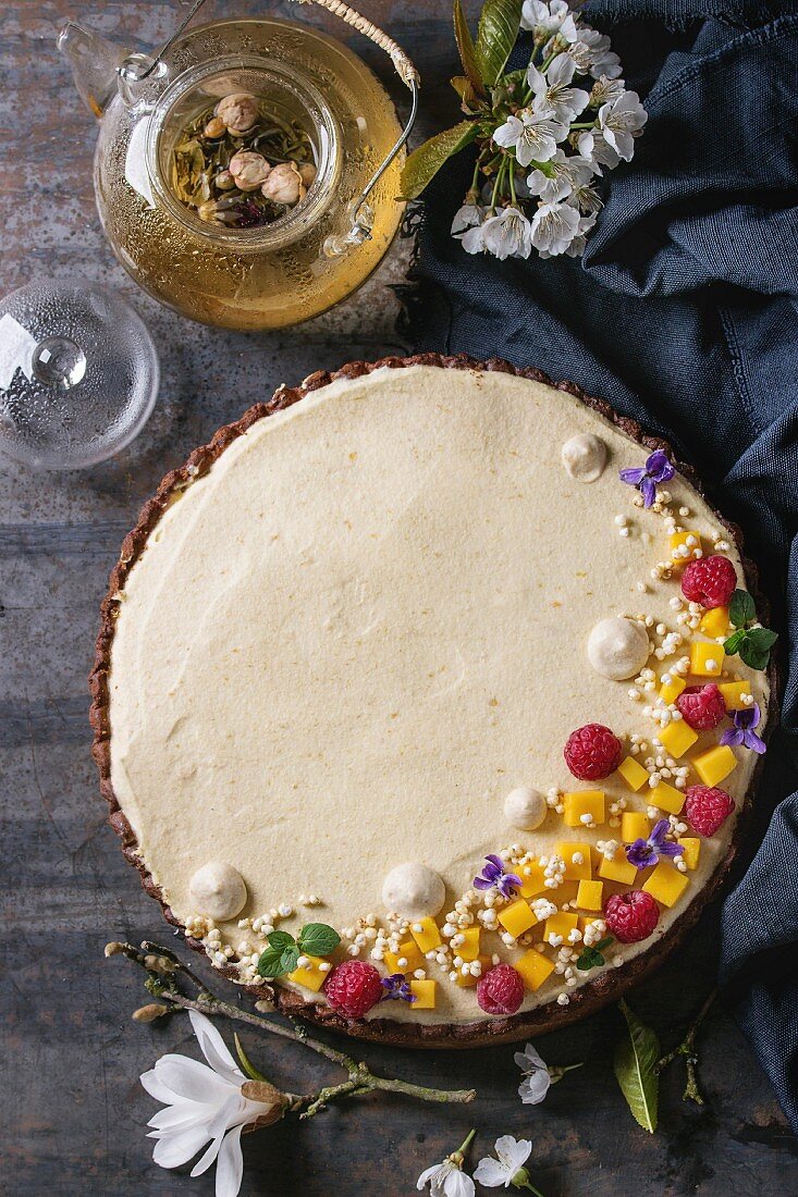 Homemade chocolate tart decorated by mango, raspberries, mint, puffed rice and edible flowers