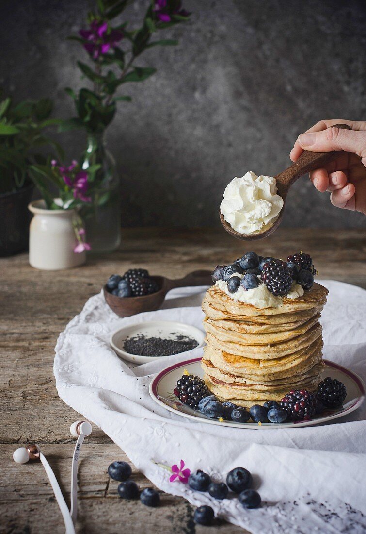 A stack of ricotta pancakes with berries and cream on a rustic wooden table