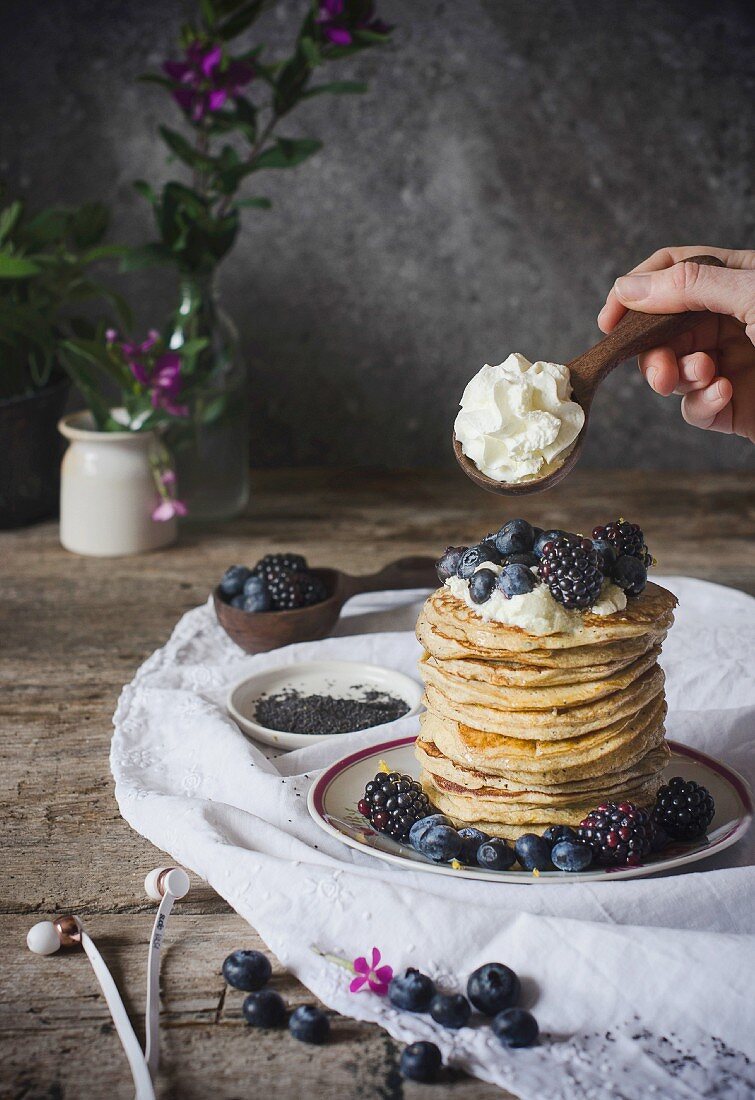 Ein Stapel Ricotta-Pancakes mit Beeren und Sahne auf rustikalem Holztisch