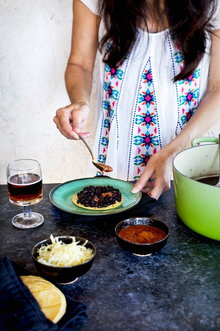 Frau gibt Salsa auf Tortillas mit schwarzen Bohnen (Mexiko)