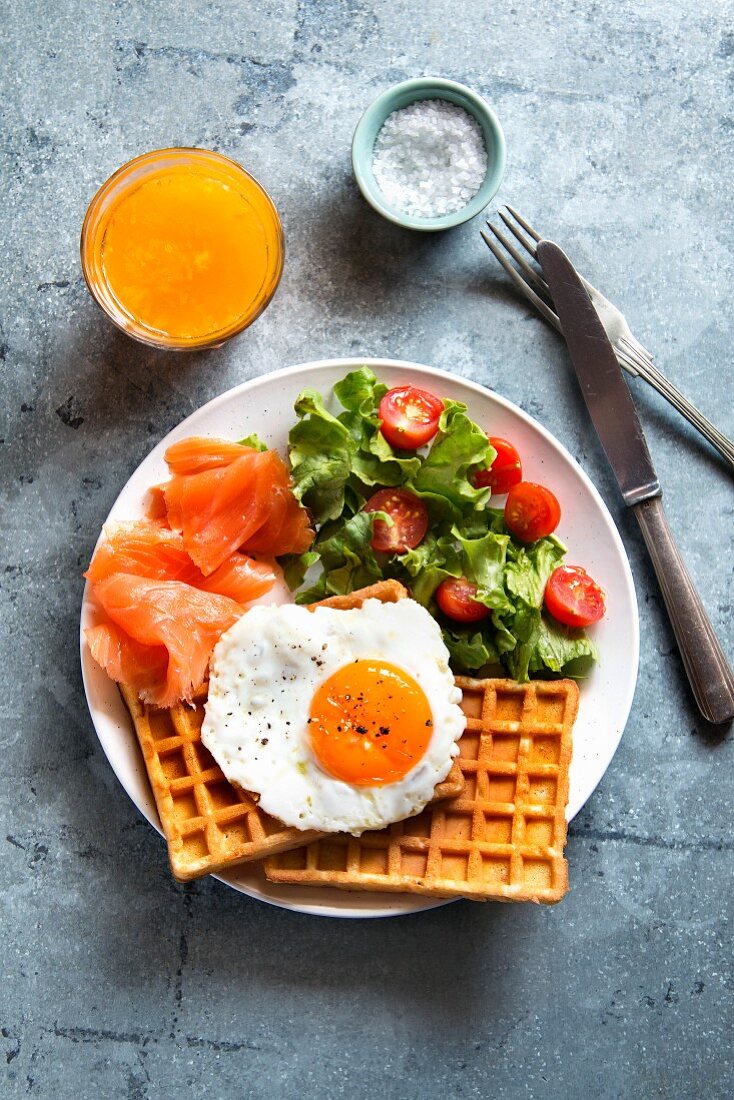 Waffles with smoked salmon, egg, salad and a glass of orange juice