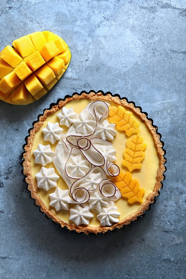 Tart with mango and coconut creamy filling, garnished with whipped cream, coconut strips and fresh mango