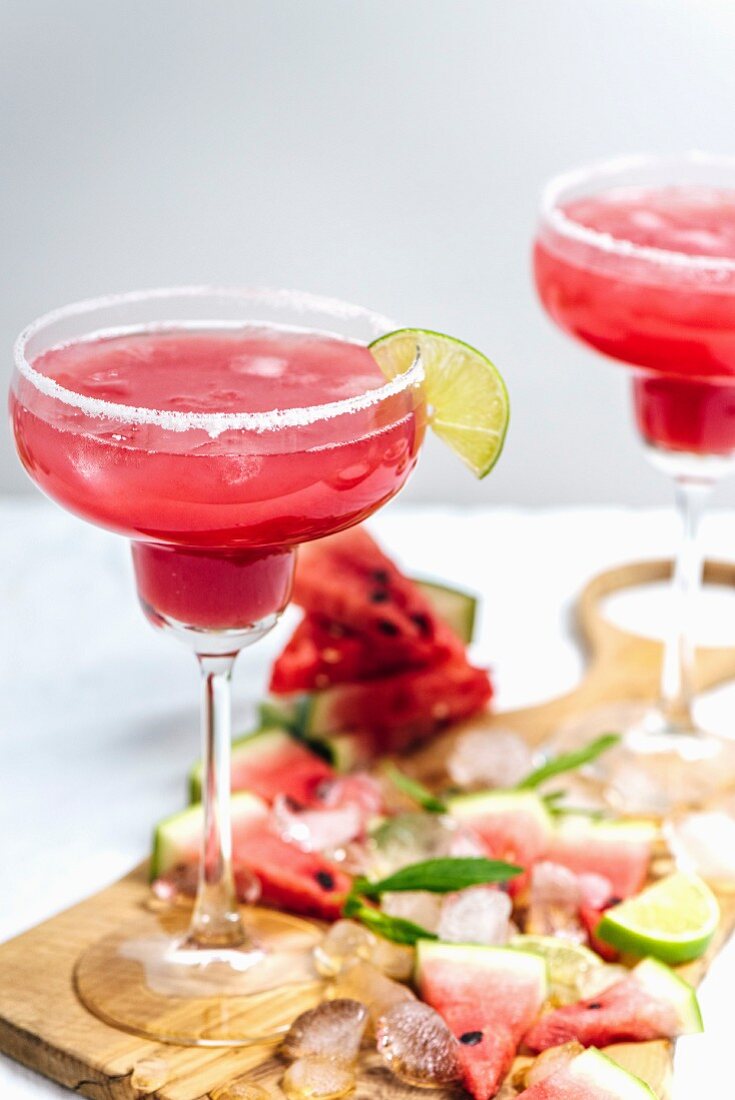 Watermelon margarita in margarita glasses standing on a wooden board