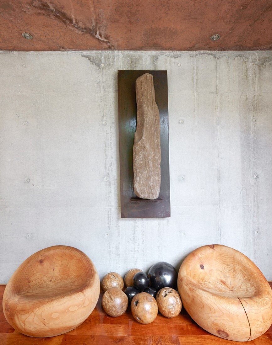 Organically formed wooden easy chairs and wooden spheres against concrete wall