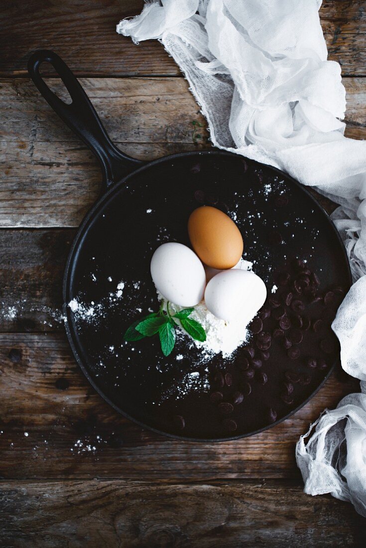 Eggs, flour and chocolate drops on a crêpe pan (seen from above)