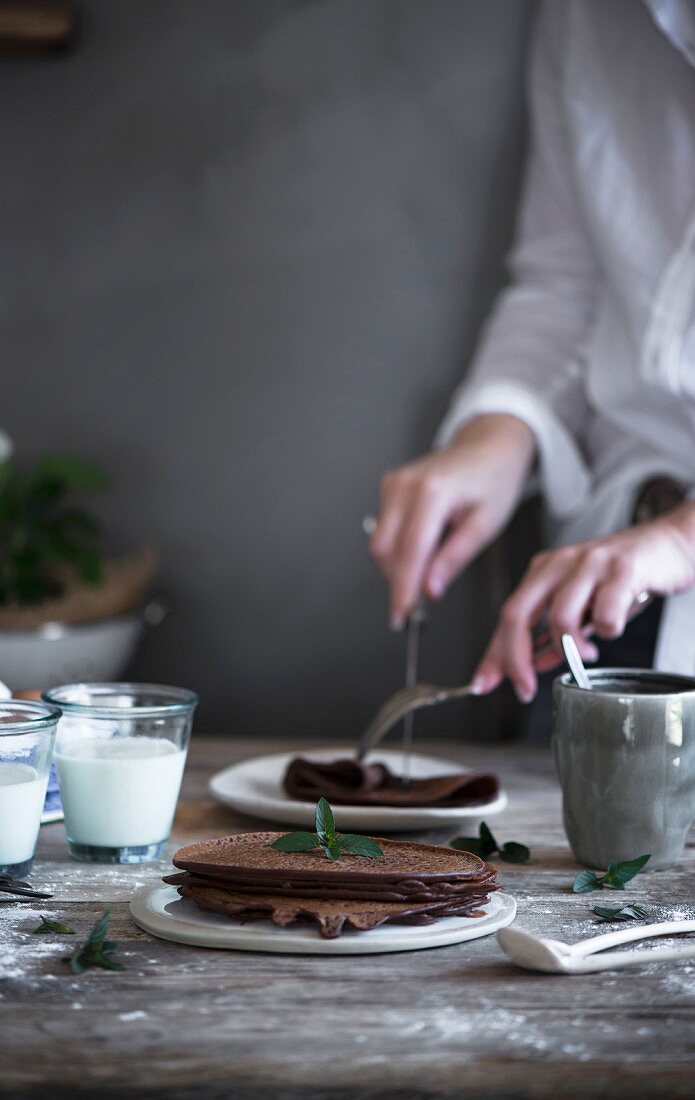 A woman cutting a chocolate pancake on a rustic wooden table