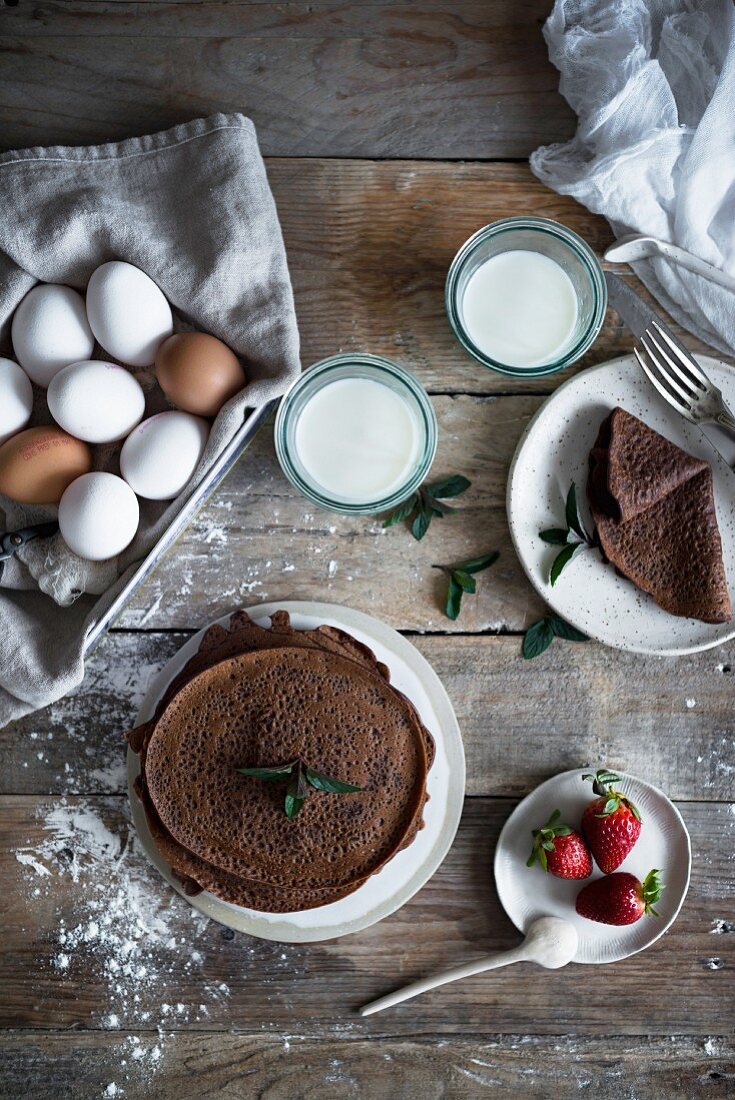 Chocolate pancakes with ingredients on a rustic wooden table (seen from above)