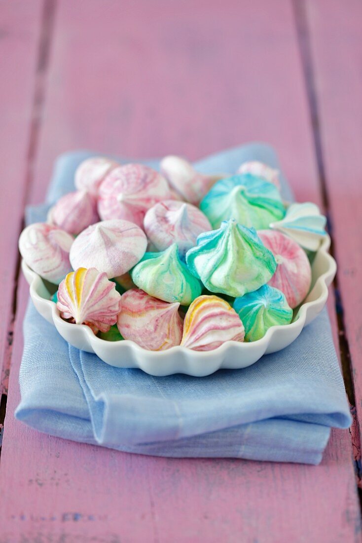 Various coloured meringue kisses in a bowl on a pink wooden background