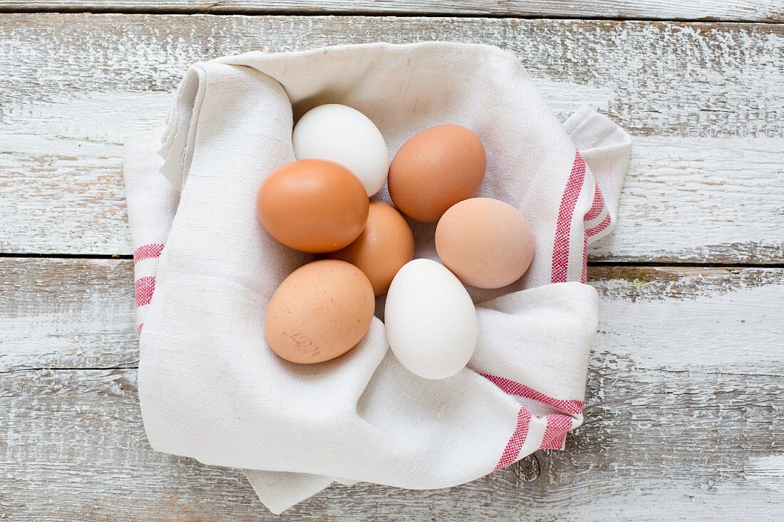 Chicken eggs in a tea towel on a wooden background (seen from above)