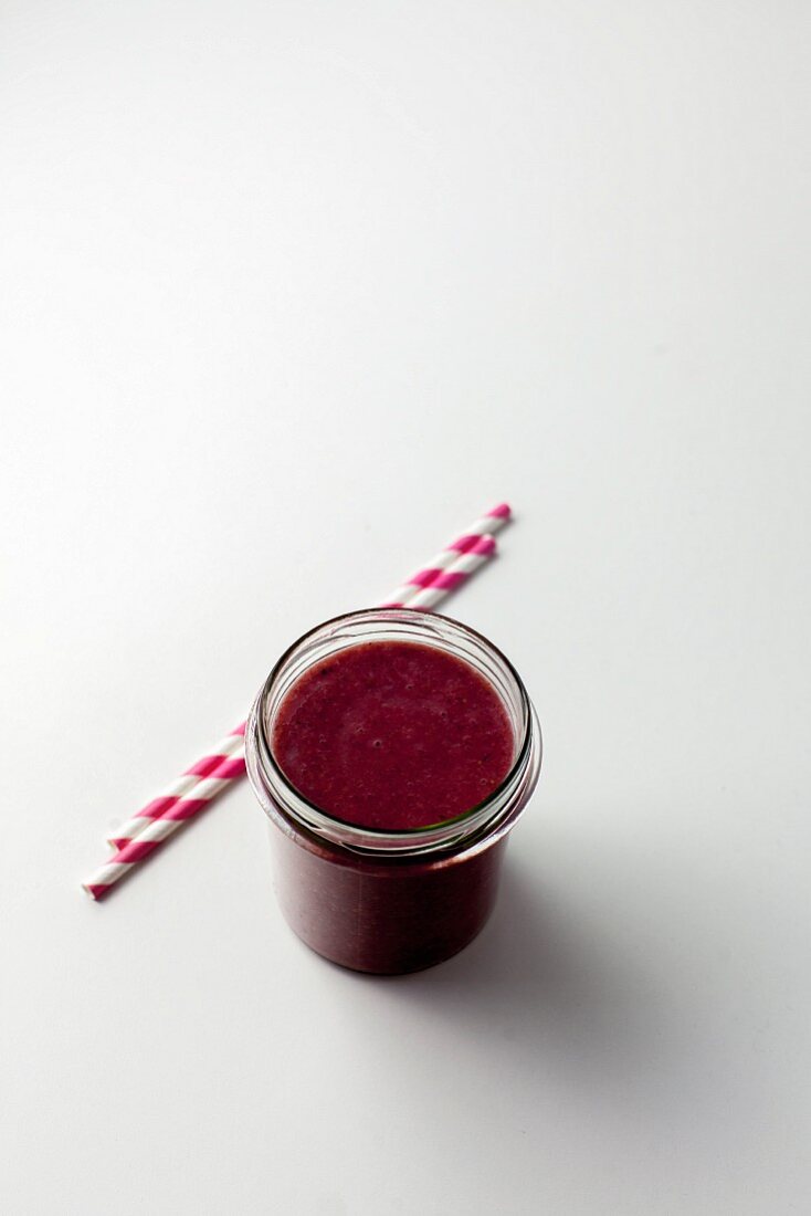 A berry smoothie in a glass with two drinking straws